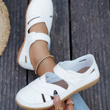 White sneakers with brown soles worn by a person on a wooden floor.