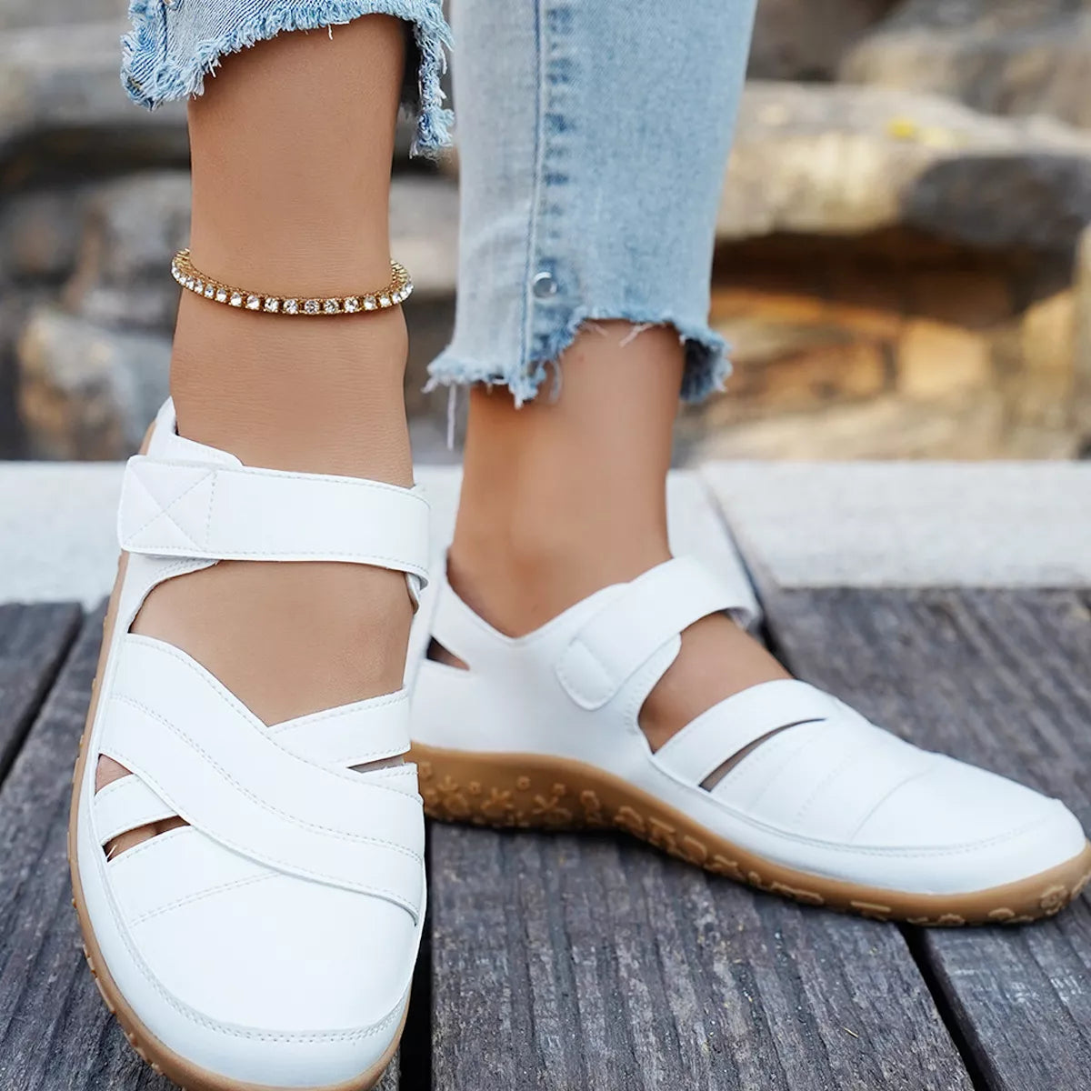 White sandals with brown soles worn on a wooden surface