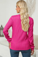 Woman wearing a cerise textured round neck long sleeve blouse with dark-wash jeans.