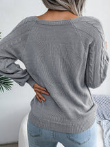 Woman wearing a charcoal cable-knit sweater with decorative buttons, paired with light-wash jeans, layered gold necklaces, and a white handbag. Perfect for cozy fall and winter outfits.
