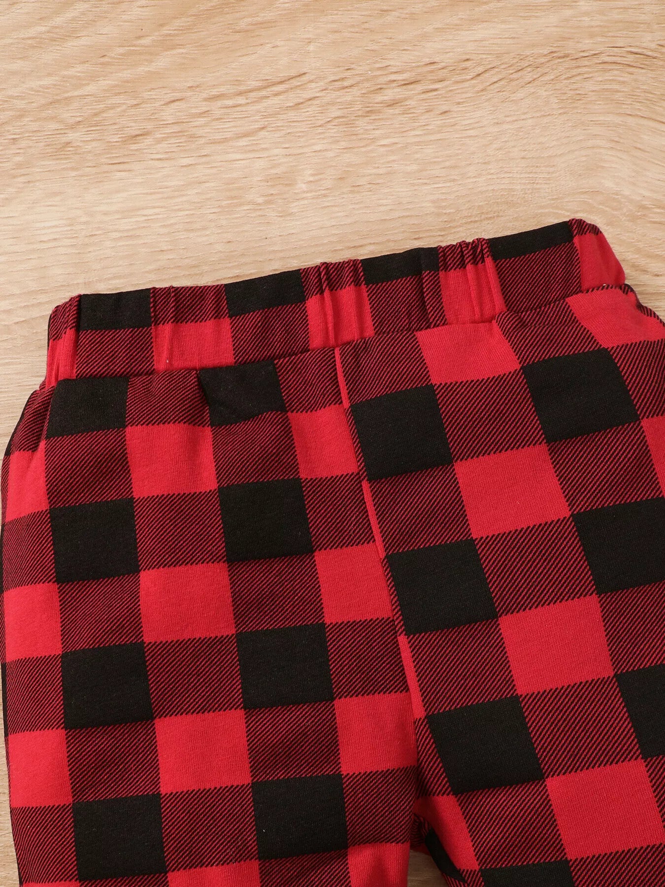 Baby girl wearing a Christmas tree graphic long sleeve top, red and black plaid ruffle pants and matching bow headband.