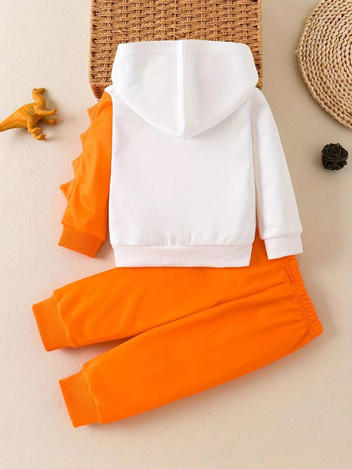 Children's white hooded sweatshirt with large orange dinosaur graphic and matching bright orange jogger-style pants.