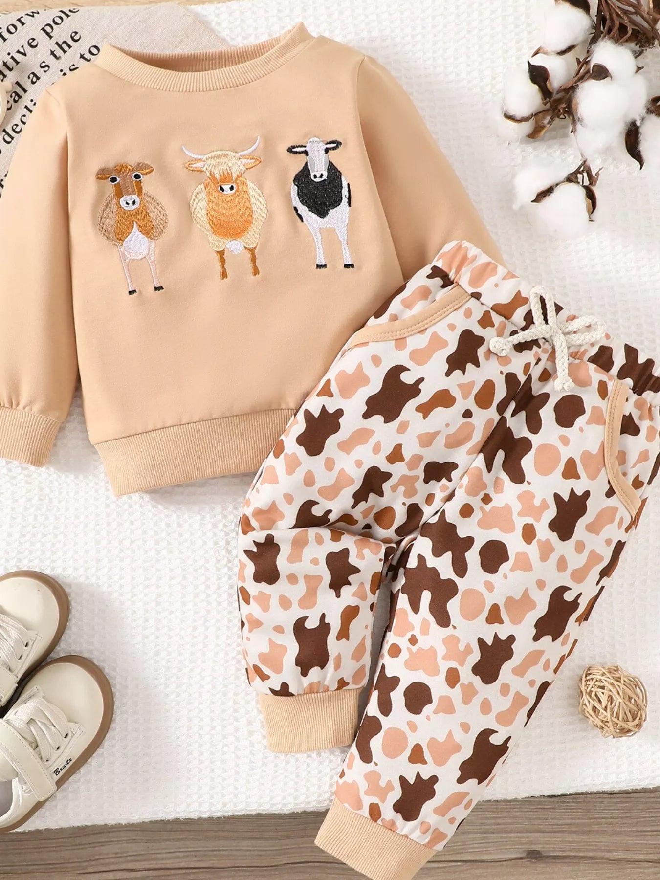 Children's two-piece farm animal outfit featuring a beige long-sleeve sweatshirt with embroidered cows and coordinating brown and cream cow-print drawstring pants.