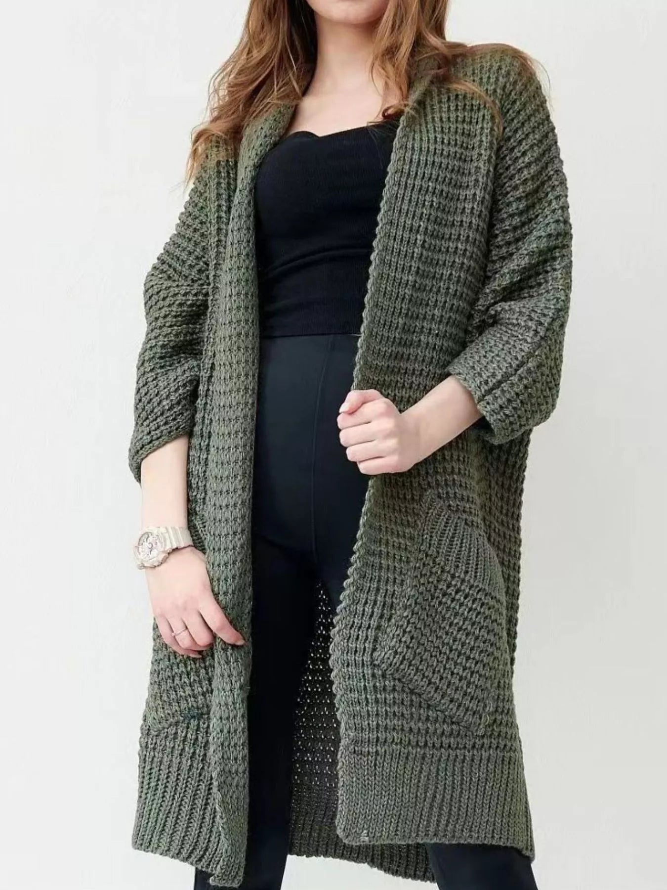 Women's army green chunky waffle knit open front cardigan with front pockets, cozy oversized fall sweater layered over a black top and leggings.