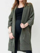 Women's army green chunky waffle knit open front cardigan with front pockets, cozy oversized fall sweater layered over a black top and leggings.