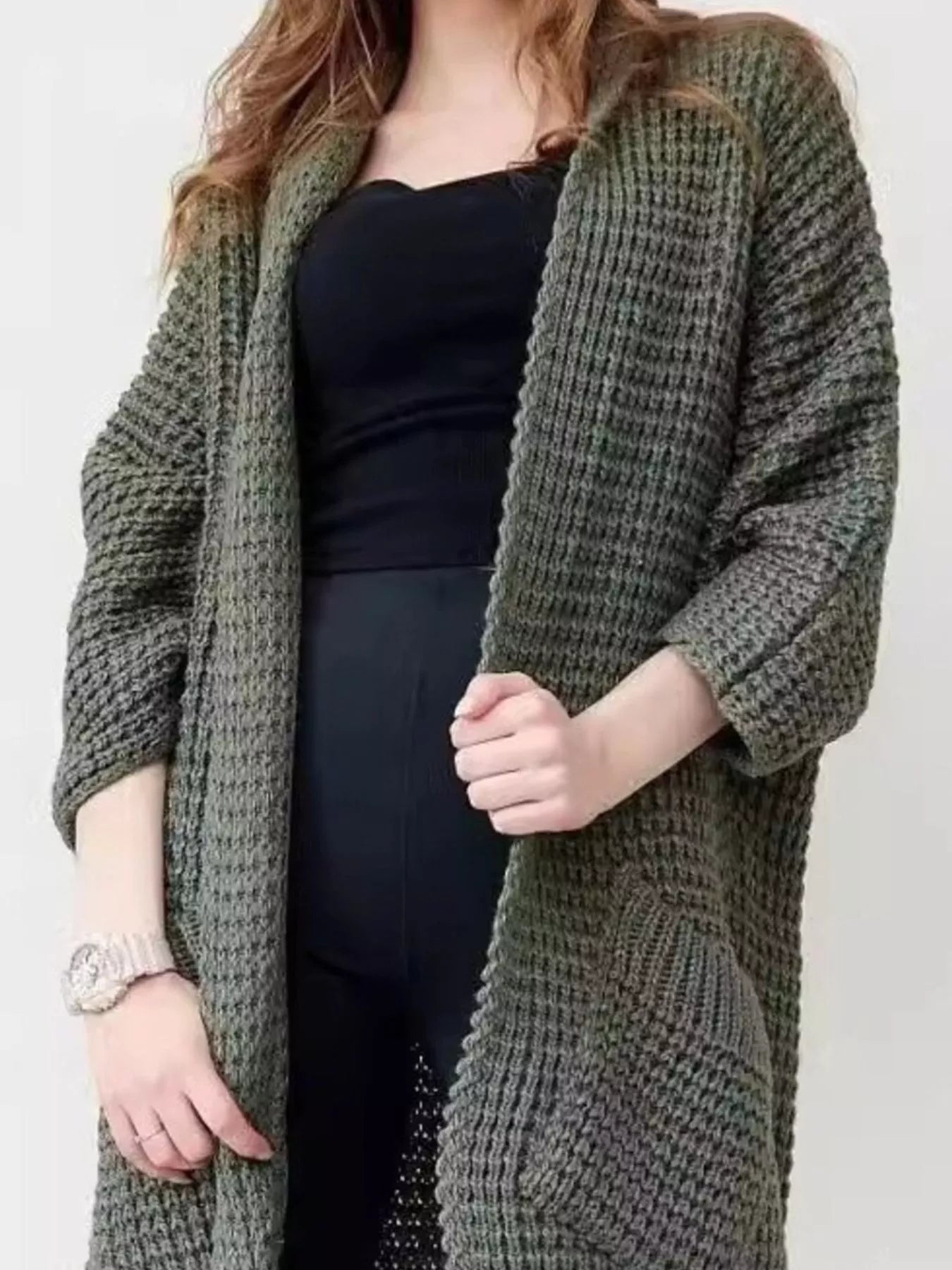 Women's army green chunky waffle knit open front cardigan with front pockets, cozy oversized fall sweater layered over a black top and leggings.