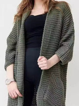 Women's army green chunky waffle knit open front cardigan with front pockets, cozy oversized fall sweater layered over a black top and leggings.