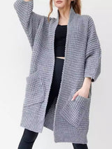 Women's gray chunky waffle knit open front cardigan with front pockets, cozy oversized fall sweater layered over a black top and leggings.