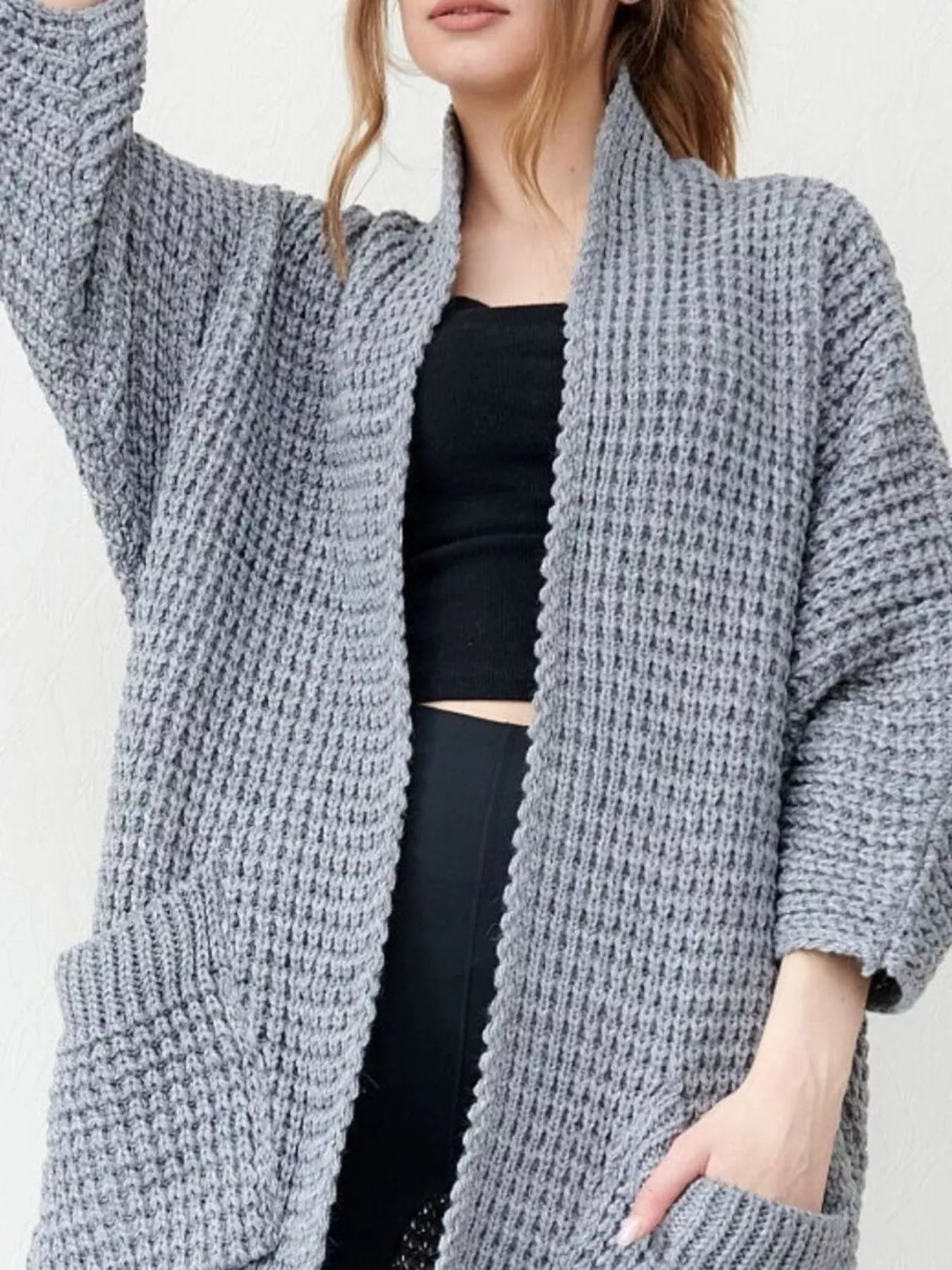 Women's gray chunky waffle knit open front cardigan with front pockets, cozy oversized fall sweater layered over a black top and leggings.