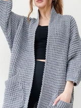 Women's gray chunky waffle knit open front cardigan with front pockets, cozy oversized fall sweater layered over a black top and leggings.