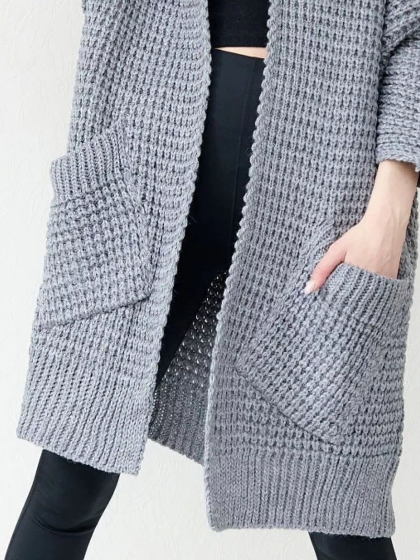 Women's gray chunky waffle knit open front cardigan with front pockets, cozy oversized fall sweater layered over a black top and leggings.
