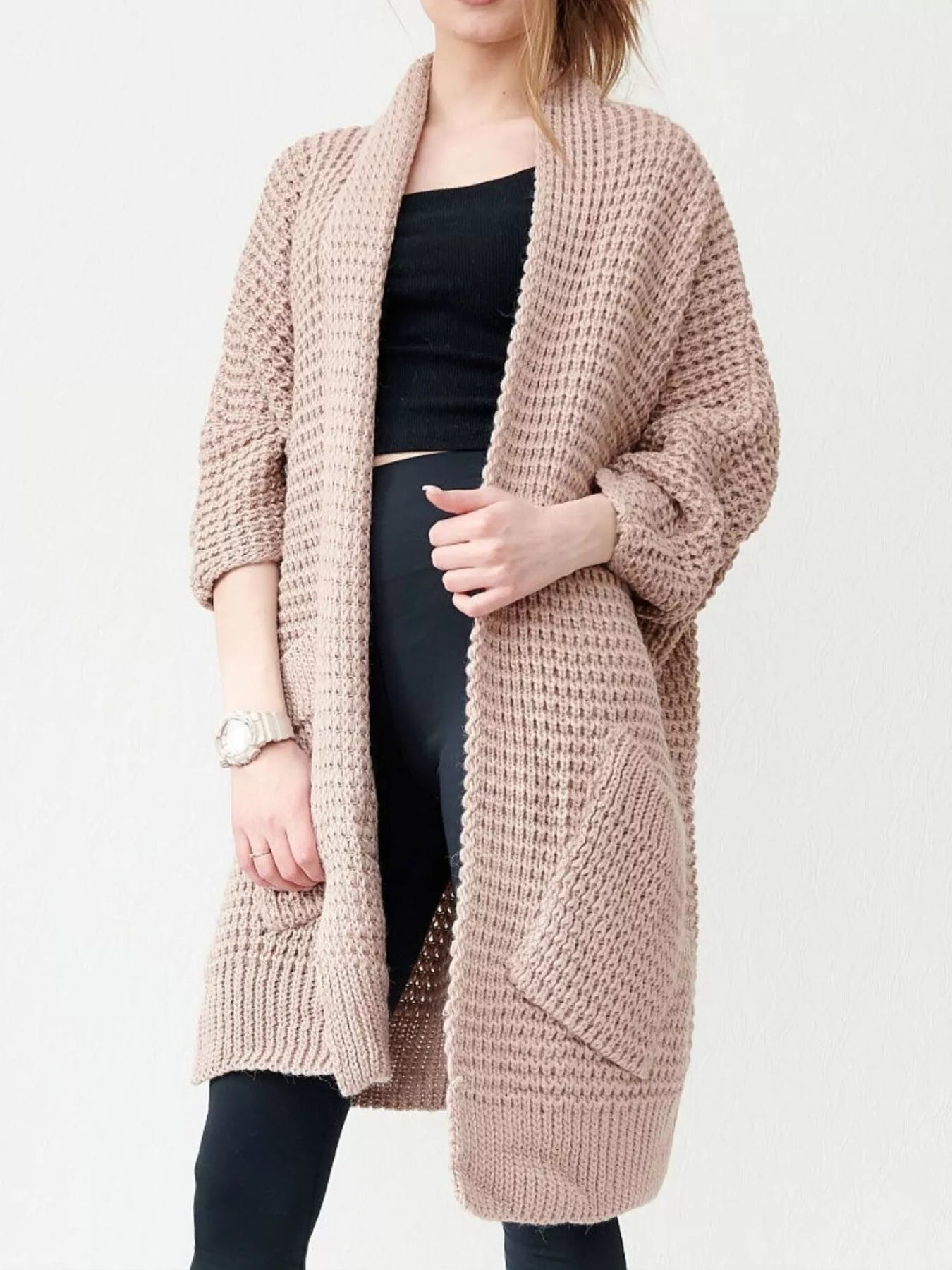 Women's khaki color chunky waffle knit open front cardigan with front pockets, cozy oversized fall sweater layered over a black top and leggings.