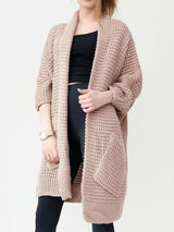 Women's khaki color chunky waffle knit open front cardigan with front pockets, cozy oversized fall sweater layered over a black top and leggings.