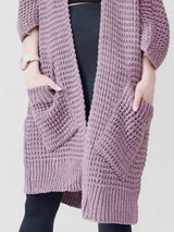 Women's purple chunky waffle knit open front cardigan with front pockets, cozy oversized fall sweater layered over a black top and leggings.
