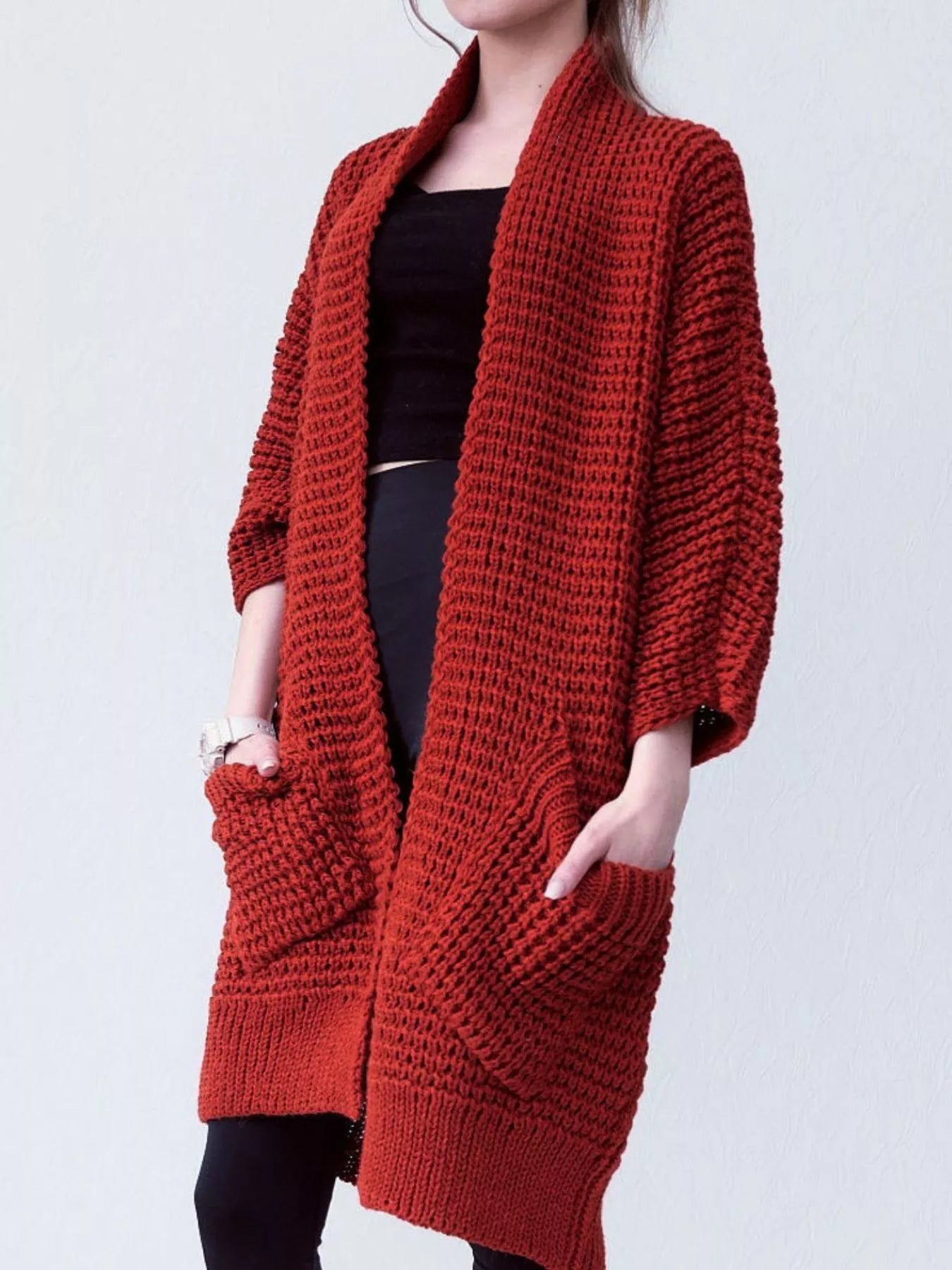 Women's red chunky waffle knit open front cardigan with front pockets, cozy oversized fall sweater layered over a black top and leggings.