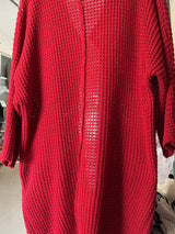 Women's red chunky waffle knit open front cardigan with front pockets, cozy oversized fall sweater layered over a black top and leggings.