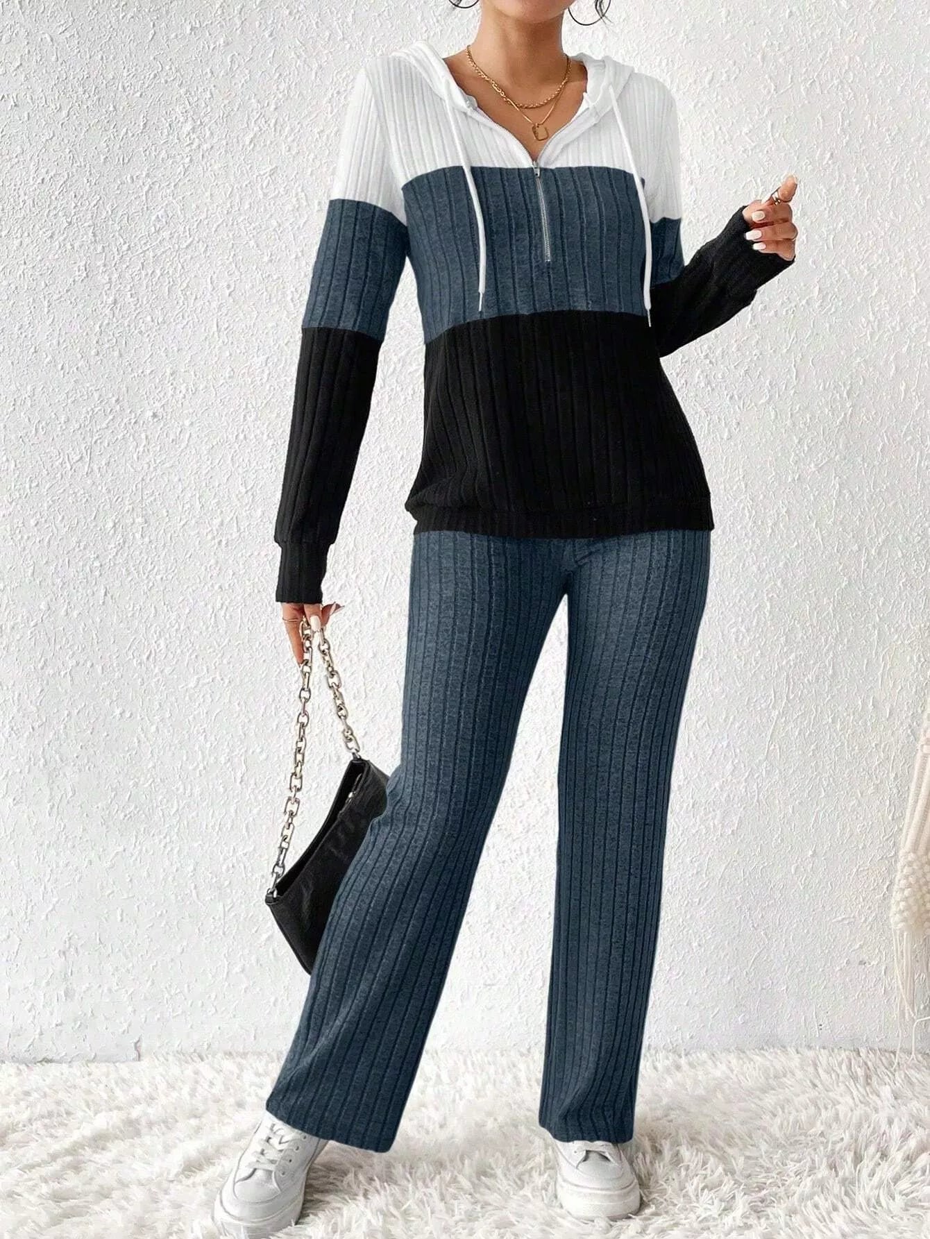 Woman wearing a dark blue, black and white color block half zip hooded top with matching ribbed-look pants.