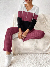 Woman wearing a deep purple, black and white color block half zip hooded top with matching ribbed-look pants.