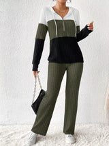 Woman wearing a moss, black and white color block half zip hooded top with matching ribbed-look pants.