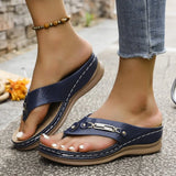 Navy blue sandals worn with light blue jeans on a stone surface.