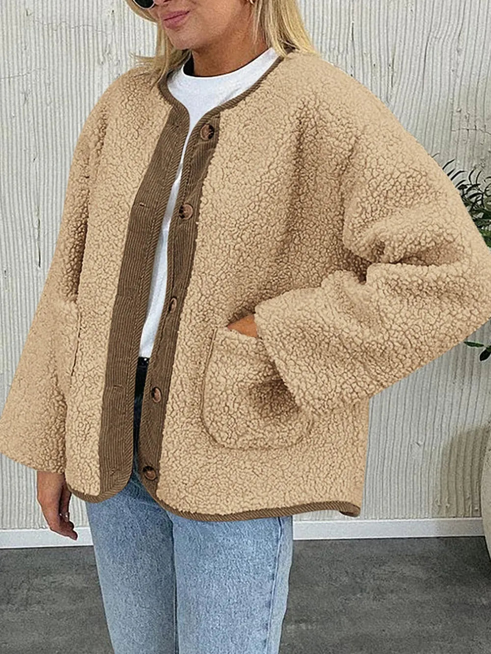 Women's tan sherpa jacket with contrasting ribbed trim, round neckline, front buttons, and patch pockets, layered over a cream sweater.