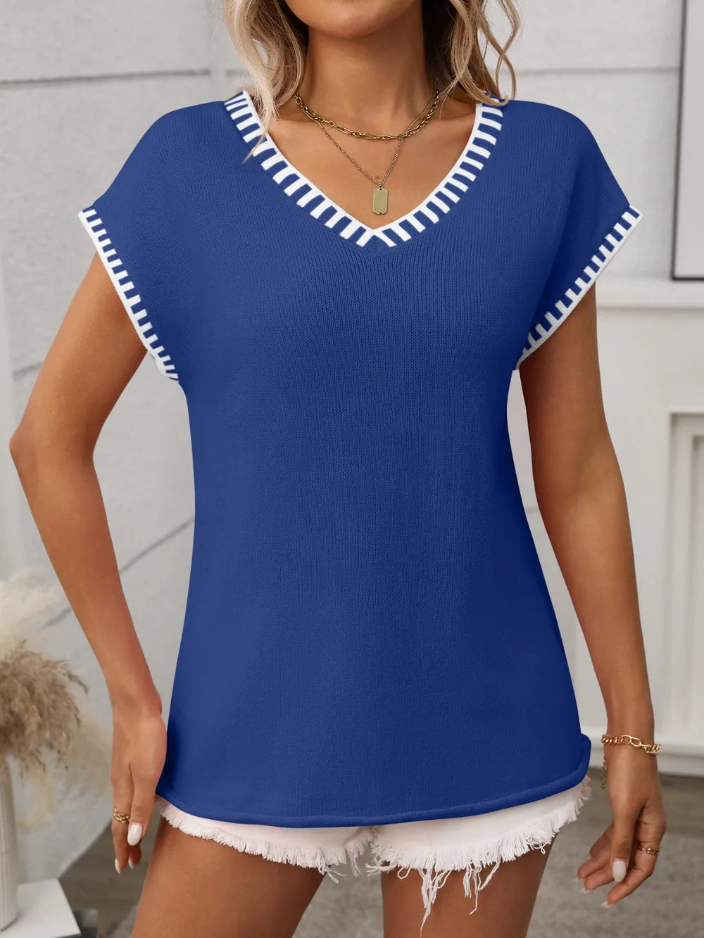 Woman wearing a royal blue short sleeve knit top with white contrast trim along the V-neckline and sleeves.