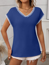 Woman wearing a royal blue short sleeve knit top with white contrast trim along the V-neckline and sleeves.
