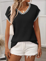Woman wearing a black short sleeve knit top with white contrast trim along the V-neckline and sleeves.