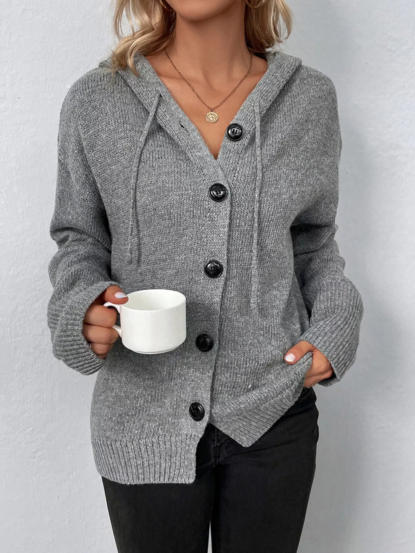 Women's gray cozy knit hooded button-down cardigan with black buttons, soft lightweight sweater paired with black pants for casual fall style.