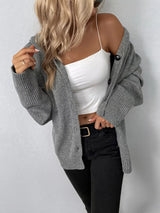 Women's gray cozy knit hooded button-down cardigan with black buttons, soft lightweight sweater paired with black pants for casual fall style.