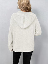 Women's white cozy knit hooded button-down cardigan with black buttons, soft lightweight sweater paired with black pants for casual fall style.