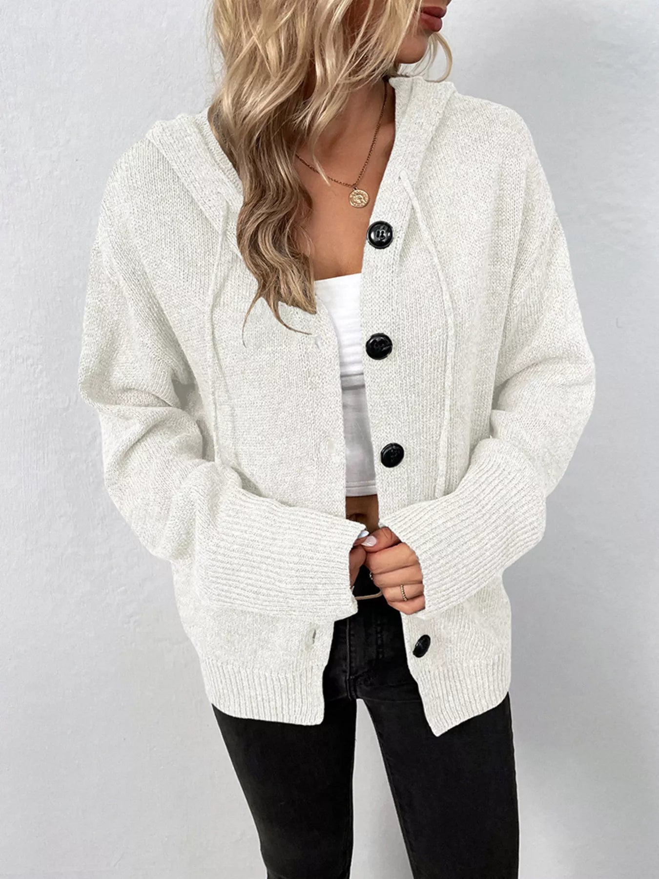 Women's white cozy knit hooded button-down cardigan with black buttons, soft lightweight sweater paired with black pants for casual fall style.