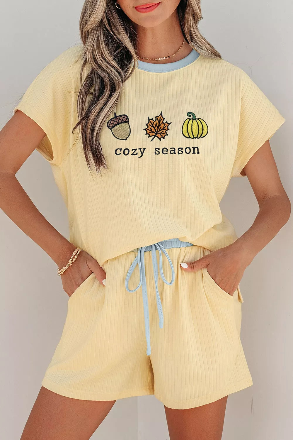 Woman wearing a Cozy Season embroidered ribbed two-piece short set featuring a relaxed fit, drawstring shorts, and fall-inspired embroidered graphics.
