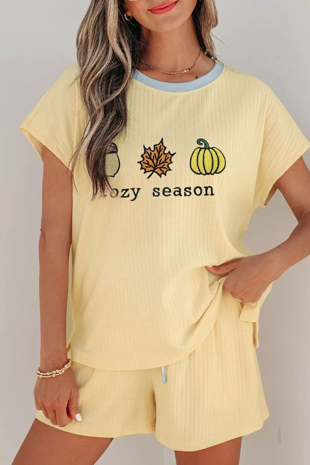 Woman wearing a Cozy Season embroidered ribbed two-piece short set featuring a relaxed fit, drawstring shorts, and fall-inspired embroidered graphics.