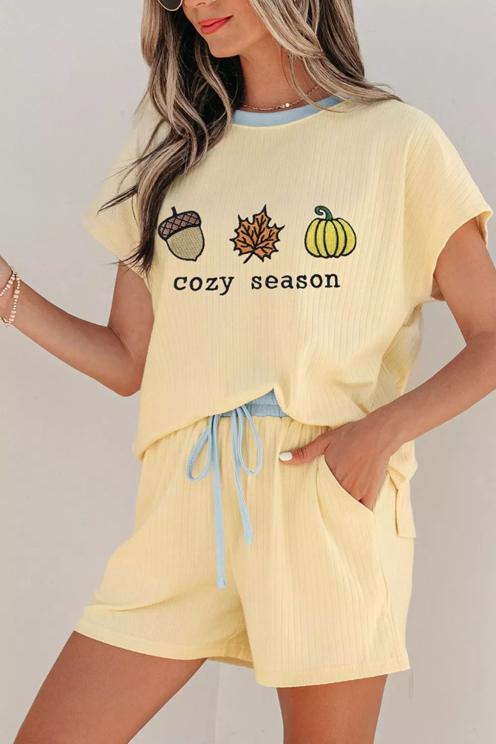 Woman wearing a Cozy Season embroidered ribbed two-piece short set featuring a relaxed fit, drawstring shorts, and fall-inspired embroidered graphics.