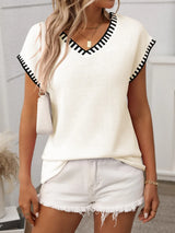 Woman wearing a cream short sleeve knit top with black contrast trim along the V-neckline and sleeves.