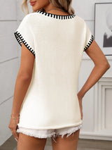 Woman wearing a cream short sleeve knit top with black contrast trim along the V-neckline and sleeves.
