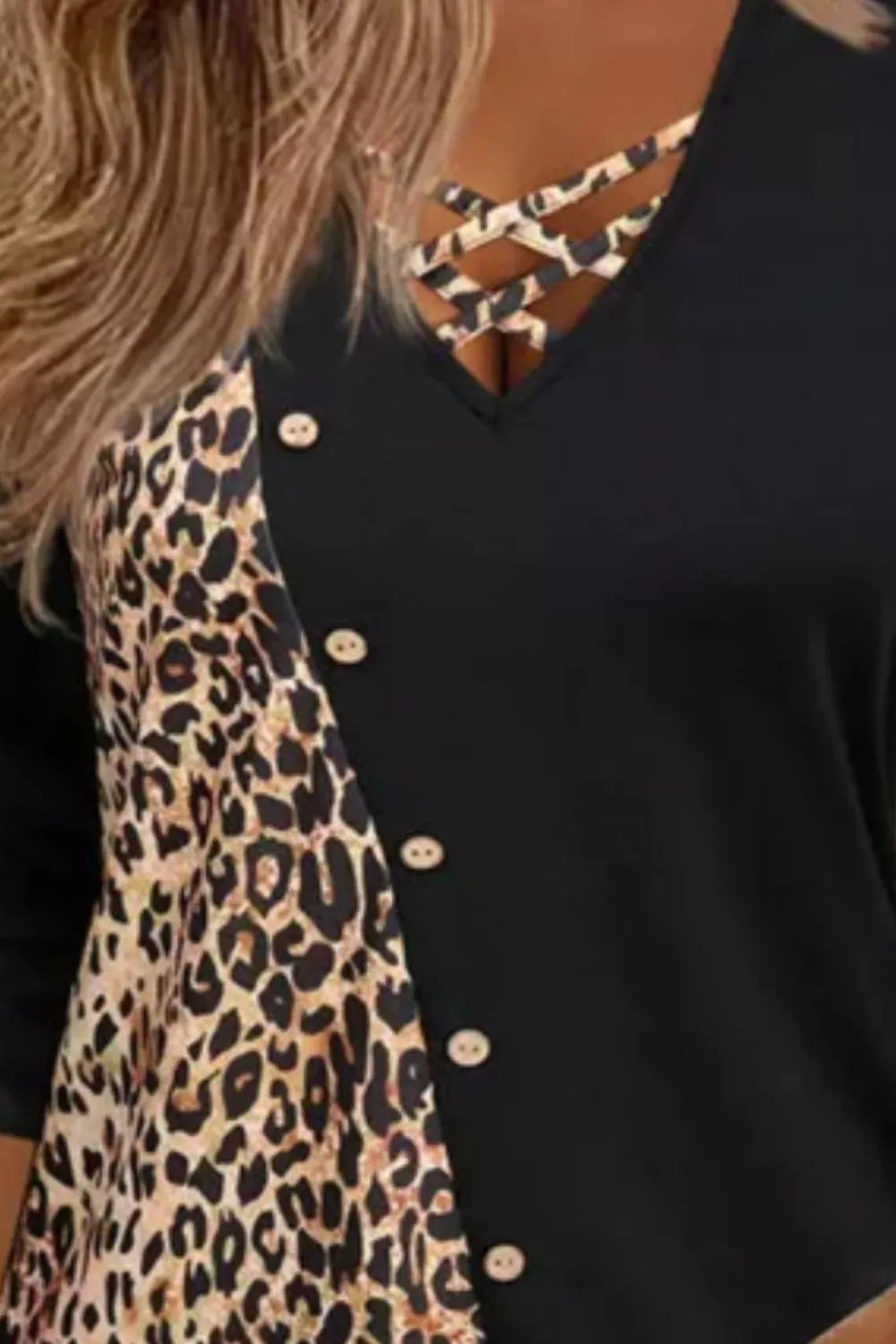 Black long-sleeve V-neck top with leopard-print color-block detailing, decorative buttons, and crisscross straps at the neckline.