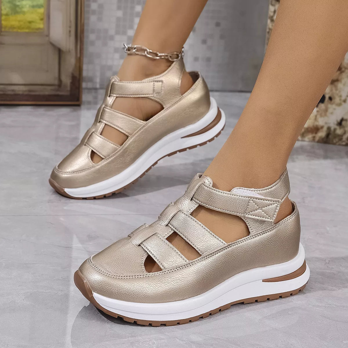 Gold sandals with white soles worn by a person on a light gray floor.