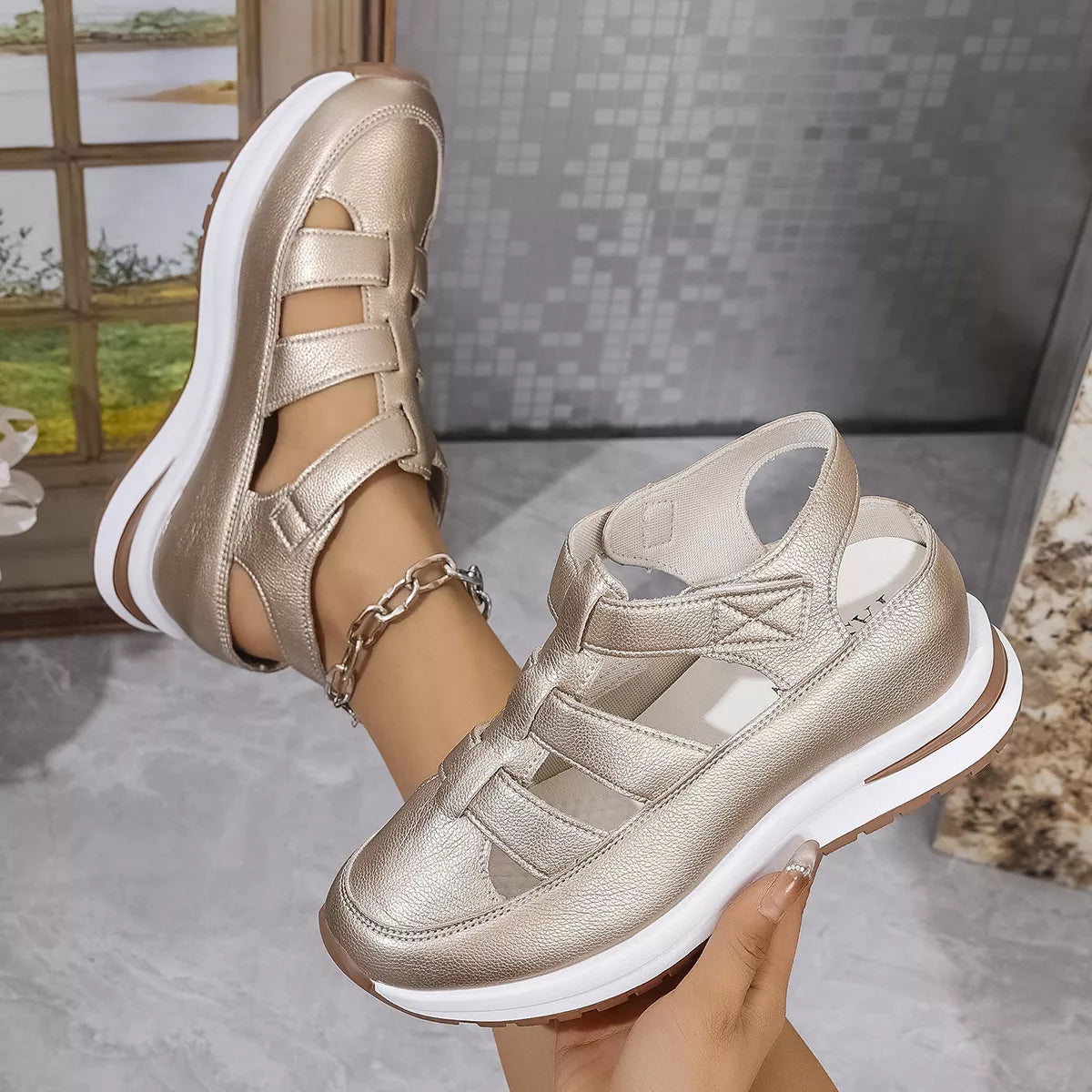 Gold sandals with white soles held by a hand against a neutral background