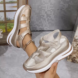 Gold sandals with white soles held by a hand against a neutral background