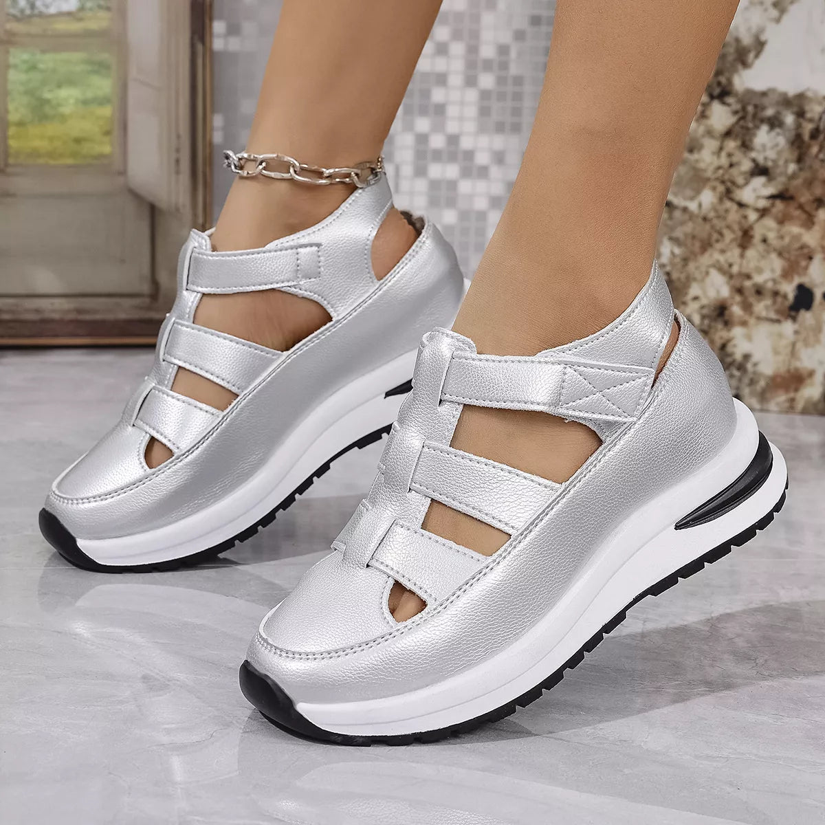 Silver strappy shoes with black soles worn by a person on a light gray surface.