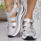 Silver sandals with black soles worn by a person on a light gray floor.