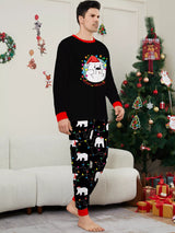 Dad wearing matching black Christmas pajamas with polar bear print, colorful holiday lights and red trim beside a Christmas tree.