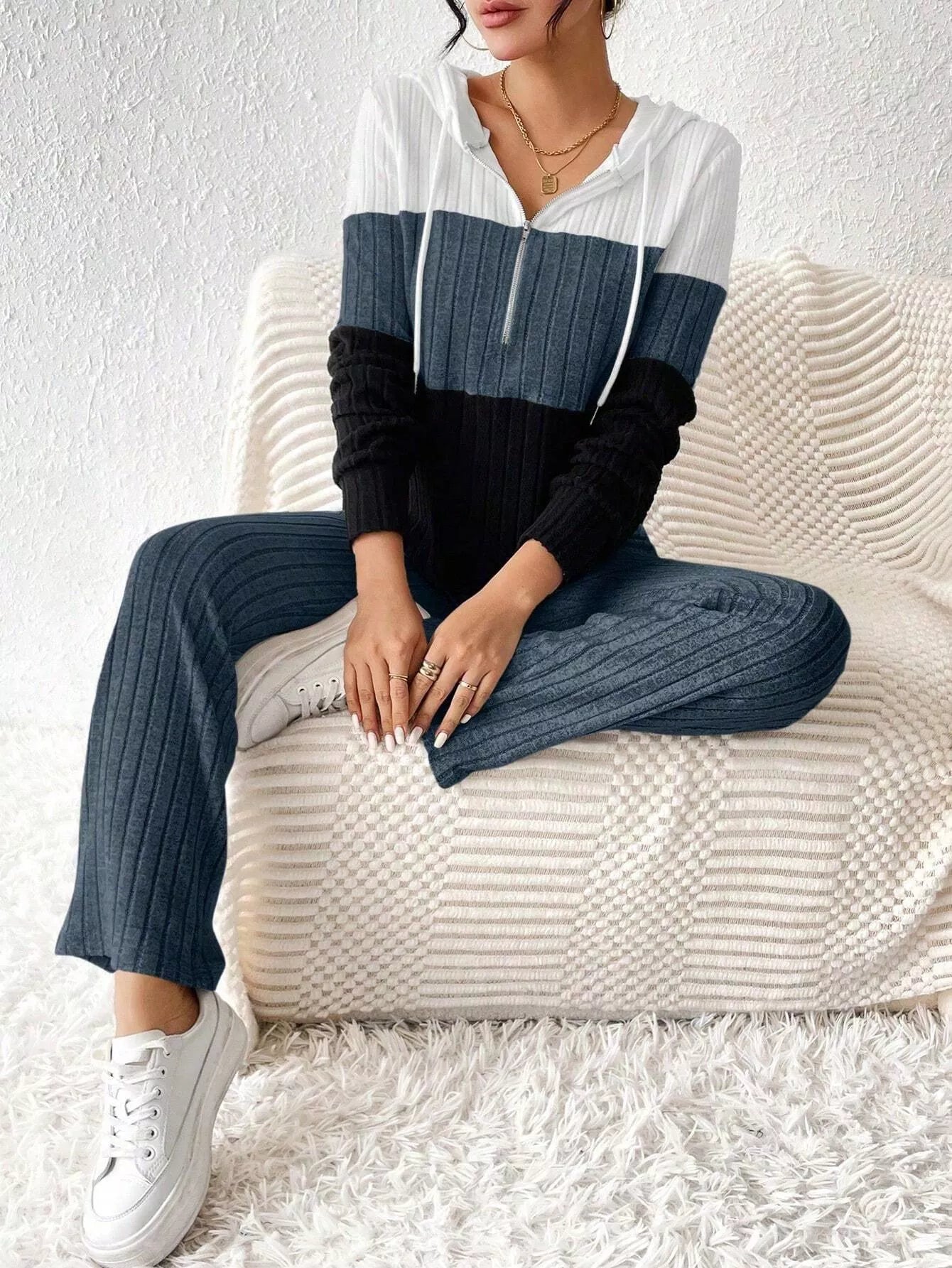 Woman wearing a dark blue, black and white color block half zip hooded top with matching ribbed-look pants.