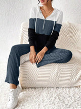 Woman wearing a dark blue, black and white color block half zip hooded top with matching ribbed-look pants.
