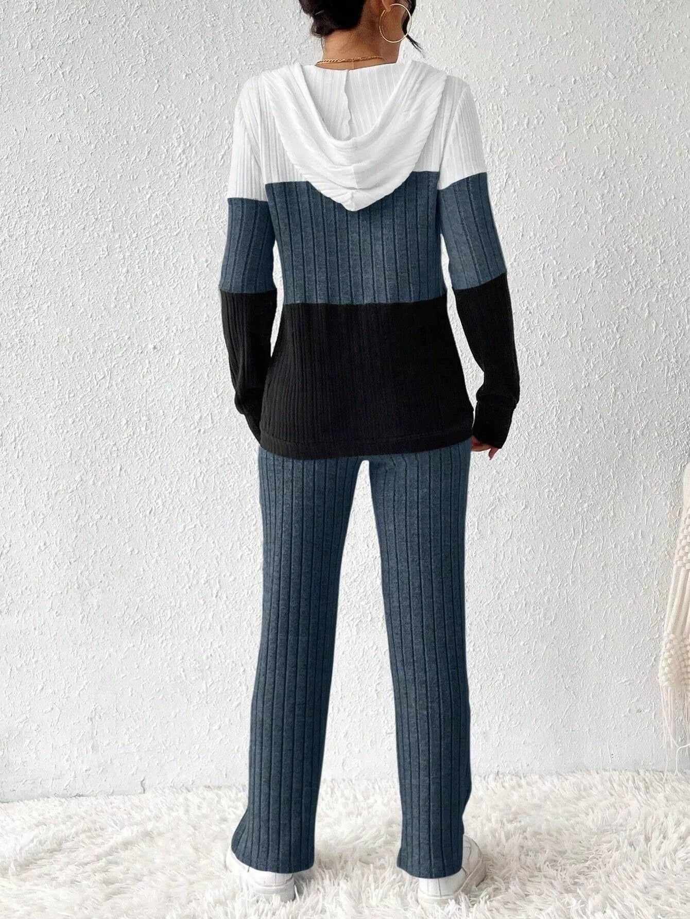 Woman wearing a dark blue, black and white color block half zip hooded top with matching ribbed-look pants.