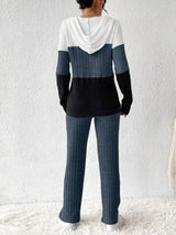 Woman wearing a dark blue, black and white color block half zip hooded top with matching ribbed-look pants.