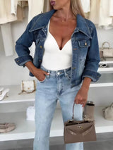 Woman wearing a dark blue cropped denim jacket over a white top with light-wash jeans and a structured handbag, styled for a chic fall outfit.