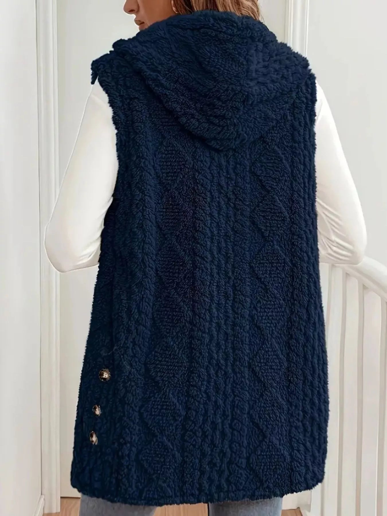 Woman wearing a dark blue hooded sherpa vest coat over a white long-sleeve top with blue jeans for a cozy fall and winter outfit.